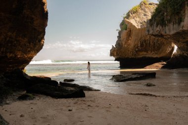Issız bir kumsalda kayalarla yalnız yürüyen bir kadın..