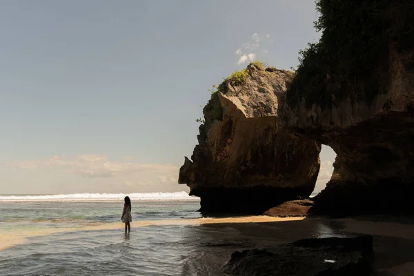 Eine Frau geht allein an einem einsamen Sandstrand mit Felsen. — Stockfoto