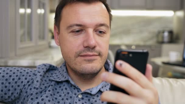 Otravný tisíciletý muž s znechuceným pohledem na displej chytrého telefonu v moderním obývacím pokoji — Stock video