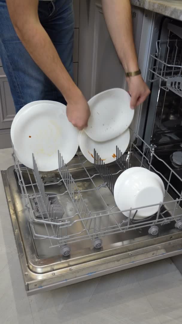 Man puts white dirty dishes in down basket of dishwasher — Stock Video