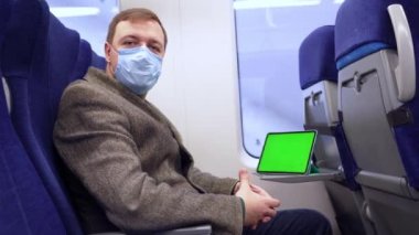 Binlerce yıllık tıbbi maskeli adam trende ve tablet bilgisayarında yeşil ekran ile geziyor.