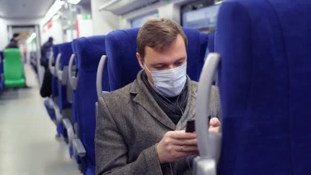 Un homme millénaire masqué qui fait la navette en train en écoutant de la musique sur son téléphone portable — Video