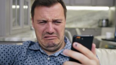 Sinirli milenyum insanı tiksinerek siniyor. Modern oturma odasındaki akıllı telefon ekranına bak.
