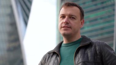 Siyah ceketli ciddi bir beyaz adam şehir manzarasında x işareti çapraz kollar portresi gösteriyor.