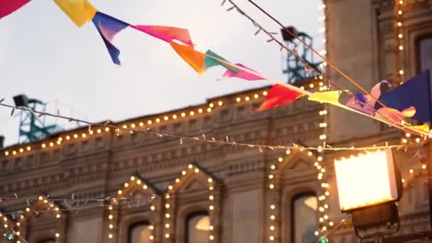 Banderas triangulares coloridas de varios colores y guirnaldas de Navidad brillantes que cuelgan en la calle en la ciudad — Vídeo de stock