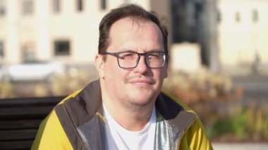 Sakin adam ahşap bankta oturuyor dinleniyor, kameraya bakıyor sonbaharda.