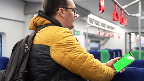 バックビューの男は電車の中で緑の画面とオンラインブラウジングでスマートフォンを見て — ストック動画