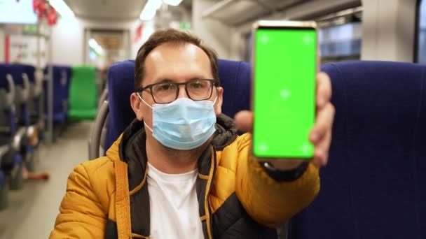 Millennial uomo in maschera cavalca sul treno e presenta telefono con chromakey alla fotocamera — Video Stock