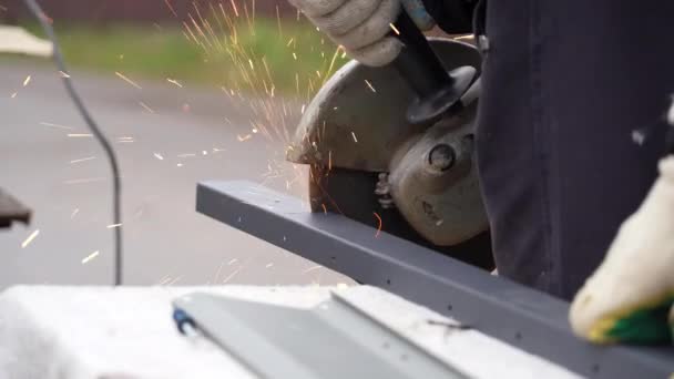 Man works circular saw. Sparks fly from hot metal. Craftsman sawing steel with disk grinder outdoors — Stockvideo