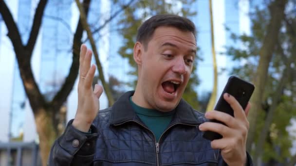 Aufgeregter Kerl schaut aufs Handy und feiert großen Gewinn — Stockvideo