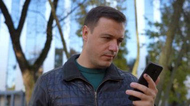 Excited guy looks at phone and celebrates big win financial good news phone near modern building