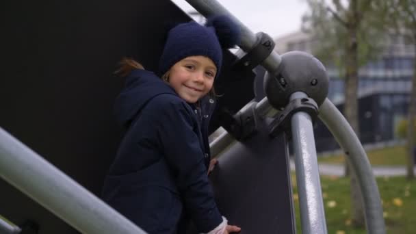 Маленька дівчинка посміхається і добре проводить час на обладнанні для скелелазіння на дитячому майданчику на відкритому повітрі — стокове відео