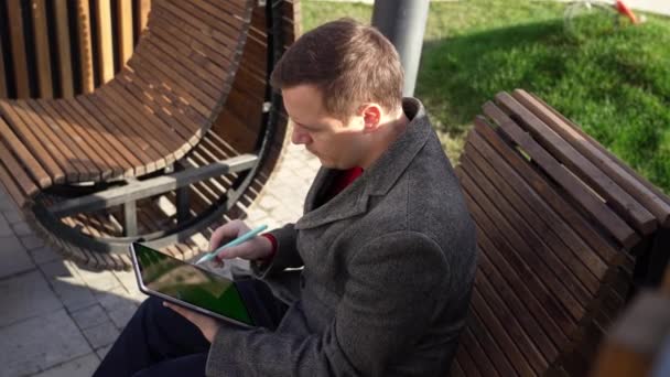 फ्रीलांसर मॅन पार्कमध्ये खंडपीठावर पेनद्वारे टॅबलेट संगणकावर इलेक्ट्रॉनिक स्वाक्षरीसह करार गाते — स्टॉक व्हिडिओ