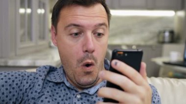 Joyful excited handsome man sitting on couch, celebrating online lottery win alone at living room