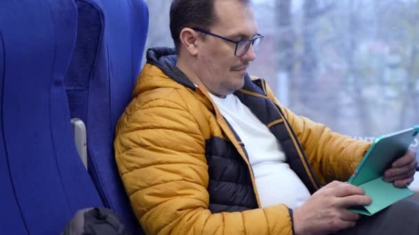 Mature positive guy in glasses texts messages using tablet computer while riding home by train — 图库视频影像