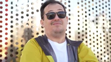 Millennial caucasian man in sunglasses leaning against perforated metal wall in city park outdoors