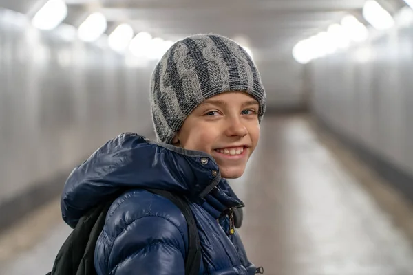 Portrait of alone happy boy in hat and jacket in underground covered walkway in city at winter — Stock Photo, Image