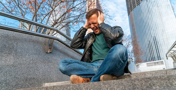 Millennial man raakt zijn hoofd door zijn handen zittend op trappen buiten in stedelijk gebied. Bezorgde man lijdt alleen in emotionele pijn zittend op stappen buiten in de stad straat — Stockfoto