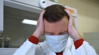 Laboratuvarda stres yüzünden baş ağrısı için beyaz önlük giyen orta yaşlı bir doktor.