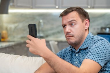 Şok olmuş bir milenyum adamı modern oturma odasındaki akıllı telefon ekranına bakar. Yönetici şaşkınlık, kötü şaka veya uygunsuz içerik ile telefon ekranına bakarak siner