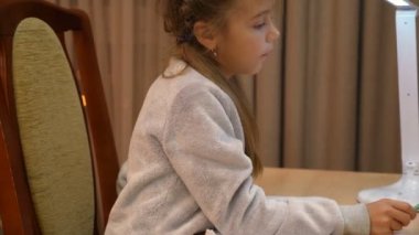 Kafkasyalı ilkokul öğrencisi. Ödev yapmak için kalem kullanıyor. Masada oturuyor.