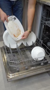 Ev işleri elektrikli aletlerle bulaşıkları yıkıyor. Adam mutfakta bulaşık makinesine tabak koyuyor.