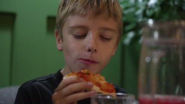 Şirin çocuk restoranda peynirli pizzadan büyük bir ısırık alıyor. Aç çocuk pizzacıda fast food yiyor.