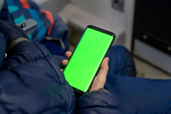 Vista posterior del teléfono inteligente del reloj del niño con la pantalla verde y la navegación en línea en tren. Prepárate para ver contenido en el teléfono celular. Teléfono digital en blanco en la mano de niño que se agita en el interior en el transporte público —  Fotos de Stock