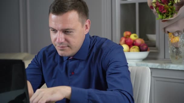Millennial guy ontspannen in de keuken met notebook op tafel, hij zit met de handen achter het hoofd — Stockvideo