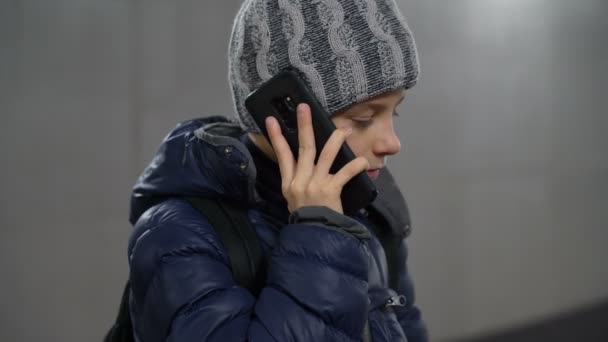 冬の街の地下の屋根付き通路で電話で話す帽子とジャケットの自信に満ちた少年 — ストック動画