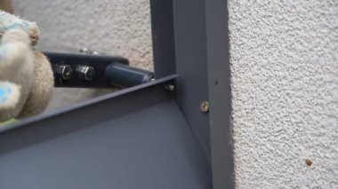 Demir parmaklıklara metal profil eklemek için perçin pense kullanan bir adamı yakından çek. Tamirci, perdelerin metal parçalarını aletle bağlıyor. Yüksek kalite 4k görüntü
