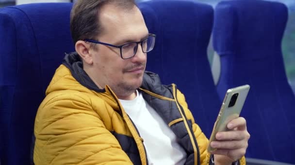 Pria dalam kacamata mencari media sosial, SMS pesan menggunakan ponsel saat berkendara pulang dengan kereta api — Stok Video