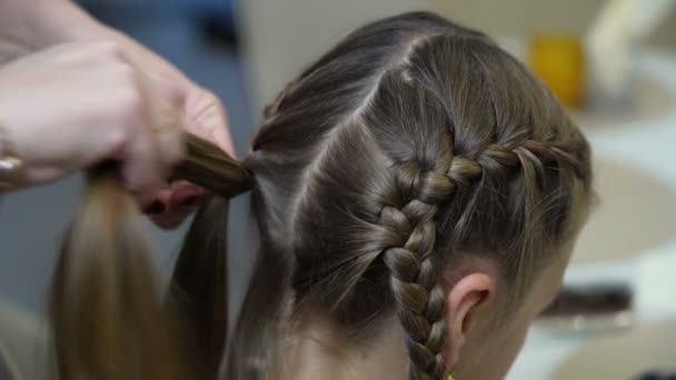 Kvinnan flätar håret på sin dotter i köket. Söt liten flicka med långt hår — Stockvideo