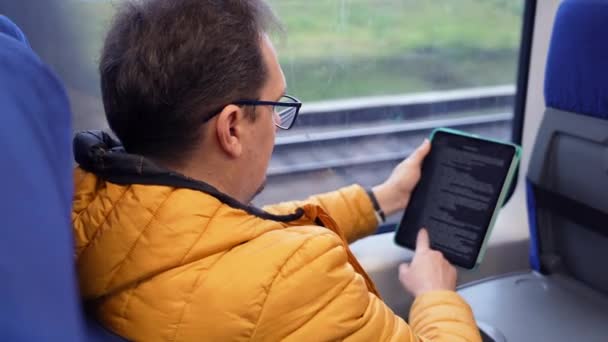 Портрет зрілого хлопця в окулярах читає електронну книгу під час їзди додому поїздом — стокове відео