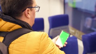 Elinde boş dijital telefon olan adam toplu taşıma araçlarında içeride dikiliyor.