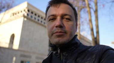 İş adamı ofis binasının önünde dikiliyor, kameraya bakıyor, anlatıyor ve konuşuyor.