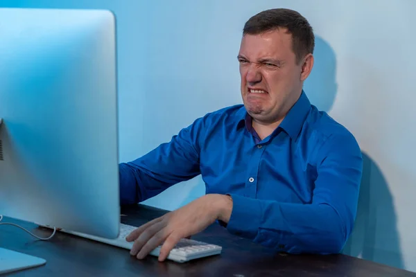 Un hombre milenario que parecía asqueado frente a su computadora en la oficina. Empresario confuso en camisa azul se encogen y mirando la pantalla con elegancia en el espacio de la oficina del negocio de puesta en marcha, trabajando en —  Fotos de Stock