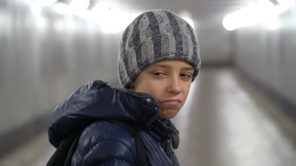 Retrato de niño triste solo en sombrero y chaqueta en pasarela cubierta subterránea en la ciudad en invierno — Vídeo de stock