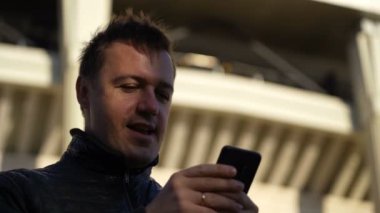 Heyecanlı erkek kazanan açık havada başarılı cep telefonunu kutluyor.