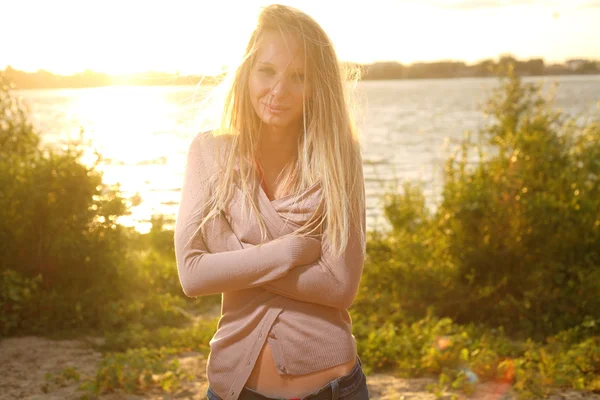 Chica cerca del río contra el sol en la puesta del sol —  Fotos de Stock