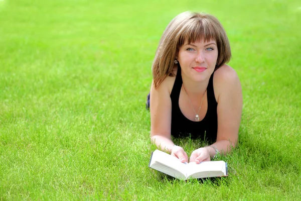 Bella giovane donna sorridente sdraiata sul libro di lettura erba — Foto Stock