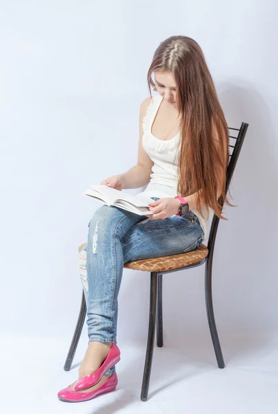 女子坐在一把椅子在读一本书的牛仔裤 — 图库照片
