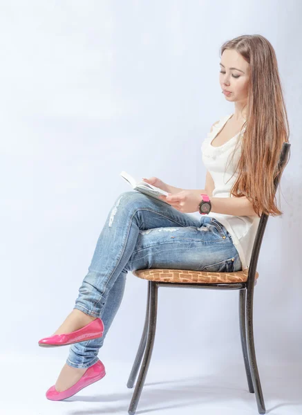 Женщина, сидящая на стуле в джинсах и читающая книгу — стоковое фото