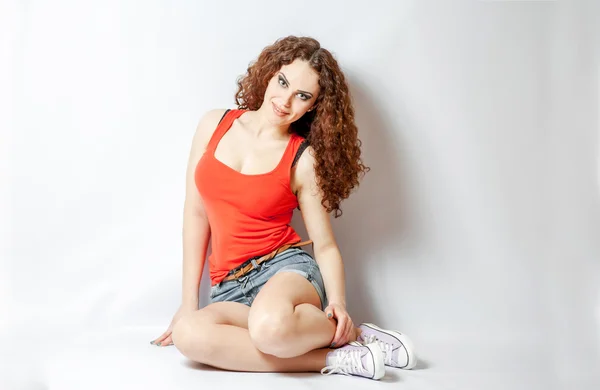 Curly brunette on white in red shirt sitting — Stock Photo, Image