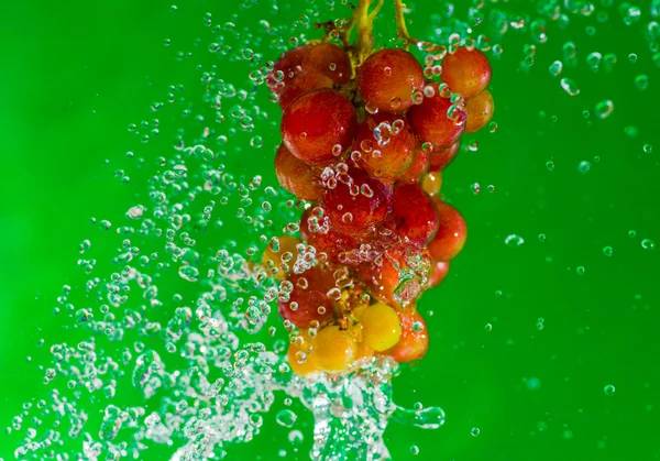 Uva roja con agua con salpicadura aislada sobre fondo verde —  Fotos de Stock