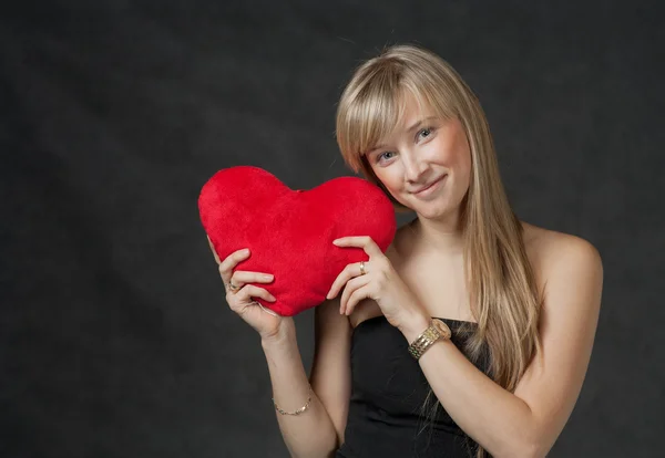 Hermosa mujer joven sosteniendo una almohada roja en forma de corazón y sonriendo — Foto de Stock