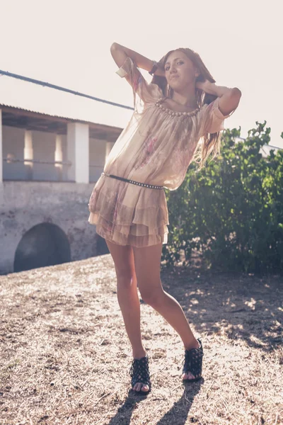 Beautiful blonde girl, dressed with a beige dress, standing in a rural bridge — Stock Photo, Image