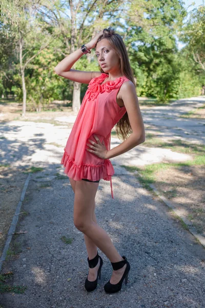 Štíhlá, krásná mladá žena v růžových šatech, stojící na zelený park — Stock fotografie