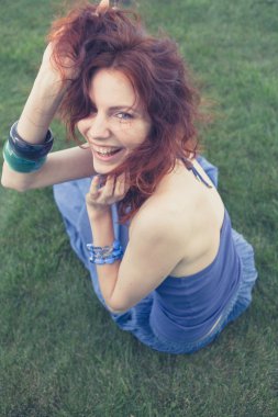 Kızıl saçlı kız yeşil çimenlerin üzerinde gülümseyen