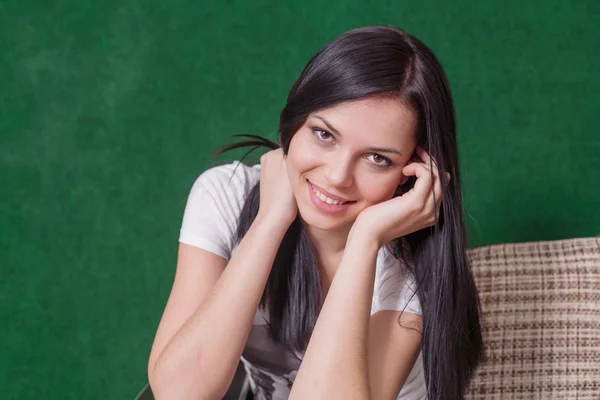 Brunette indoors sitting against green wall — Stock Photo, Image